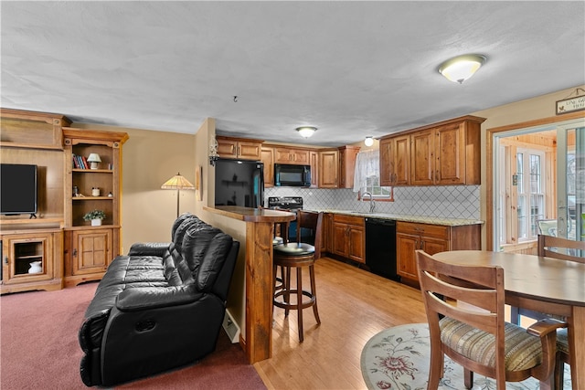 kitchen with decorative backsplash, brown cabinets, a kitchen breakfast bar, black appliances, and a sink