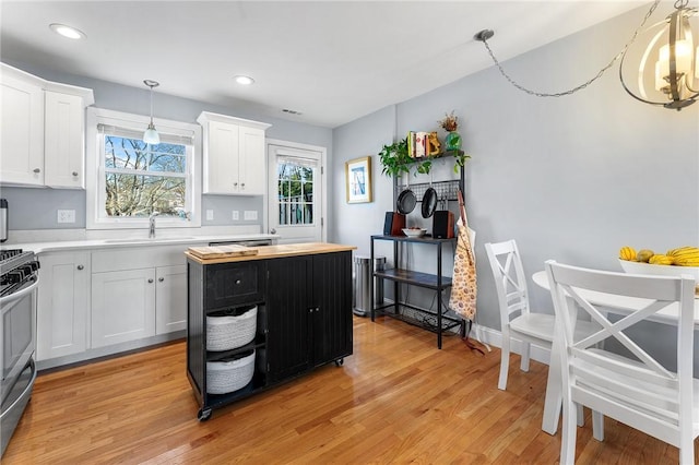 kitchen featuring a sink, gas stove, light wood-style flooring, and white cabinetry