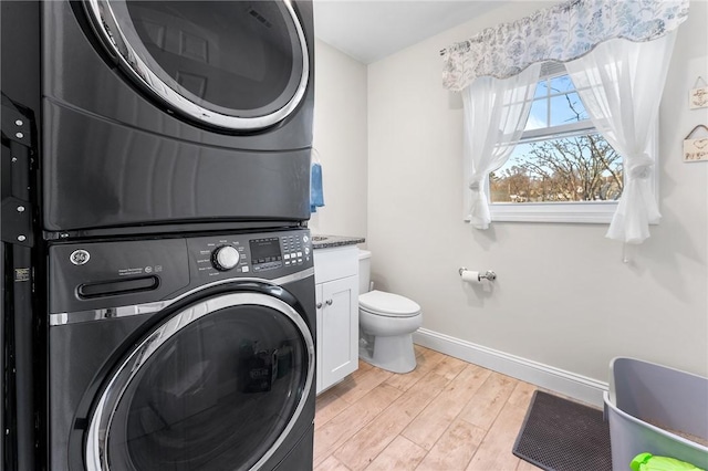 laundry area featuring laundry area, stacked washer / dryer, baseboards, and light wood-type flooring