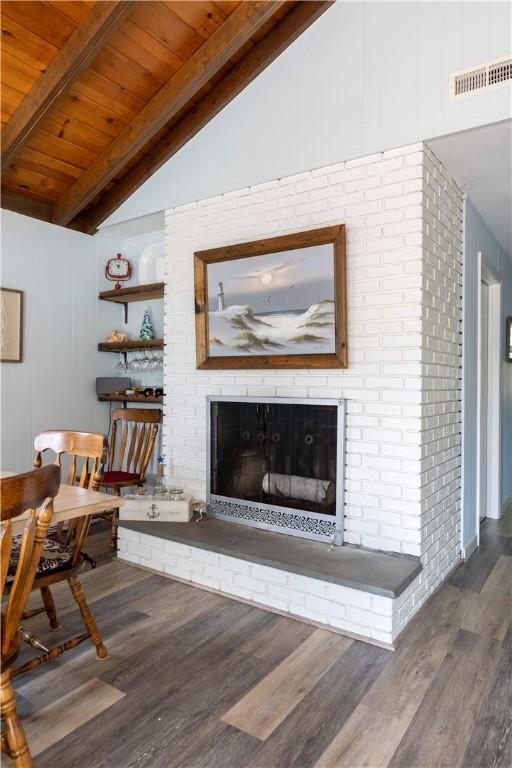 living room featuring wood finished floors, visible vents, lofted ceiling with beams, a fireplace, and wood ceiling