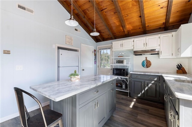 kitchen featuring visible vents, vaulted ceiling with beams, black microwave, under cabinet range hood, and freestanding refrigerator