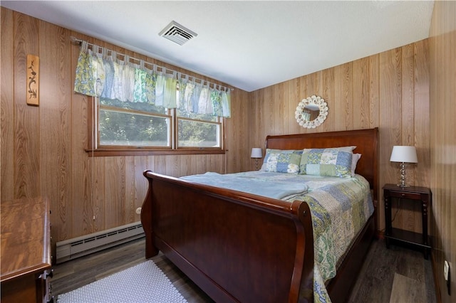 bedroom with visible vents, baseboard heating, wood finished floors, and wooden walls