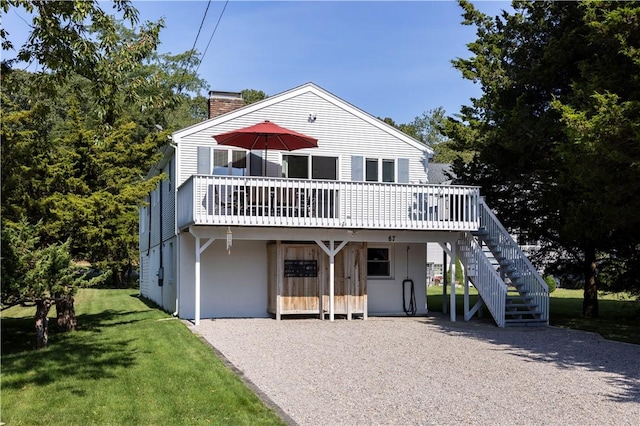 view of front of home featuring a chimney, driveway, a front yard, a wooden deck, and stairs