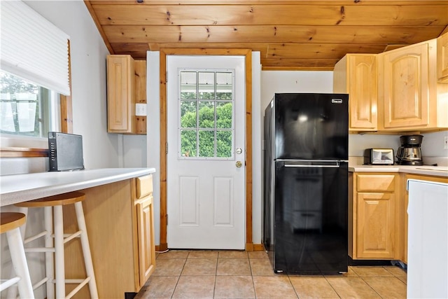 kitchen with light tile patterned flooring, light brown cabinets, and freestanding refrigerator