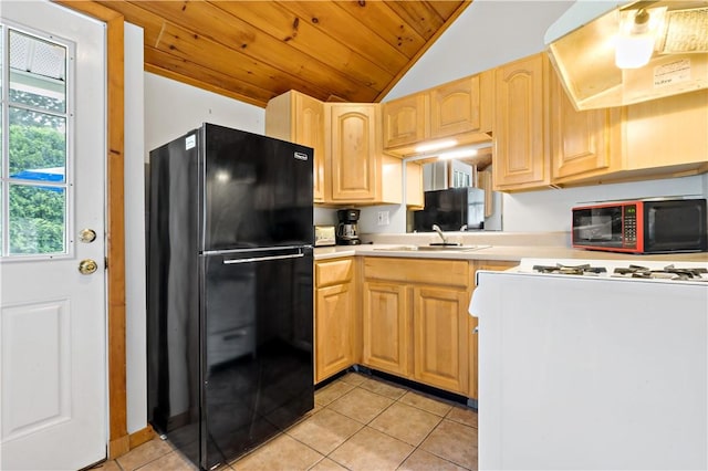 kitchen featuring under cabinet range hood, light brown cabinetry, light countertops, freestanding refrigerator, and a sink