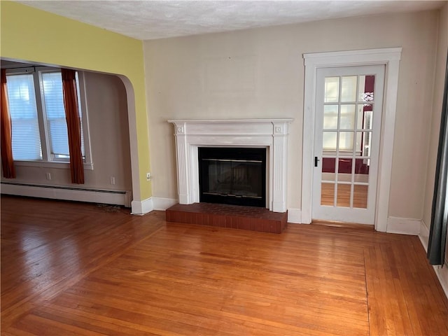 unfurnished living room with a glass covered fireplace, a baseboard heating unit, baseboards, and wood finished floors