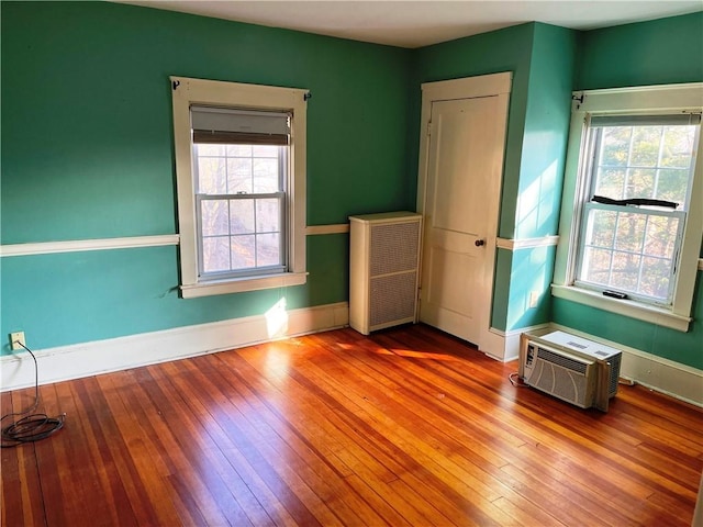 empty room featuring an AC wall unit, radiator heating unit, baseboards, and hardwood / wood-style flooring