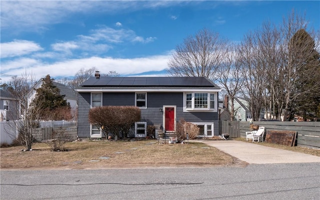 bi-level home featuring roof mounted solar panels, entry steps, and fence