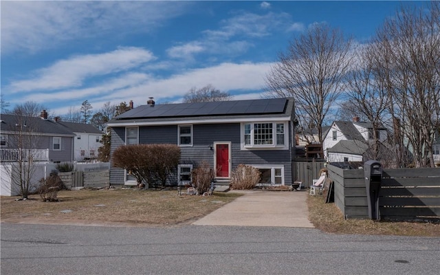 bi-level home with roof mounted solar panels, driveway, and fence