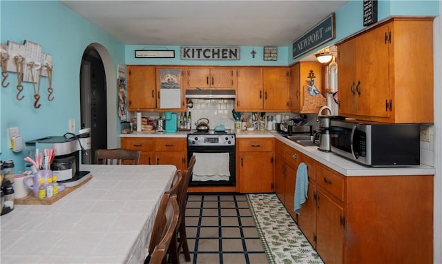 kitchen featuring under cabinet range hood, a sink, backsplash, appliances with stainless steel finishes, and brown cabinetry