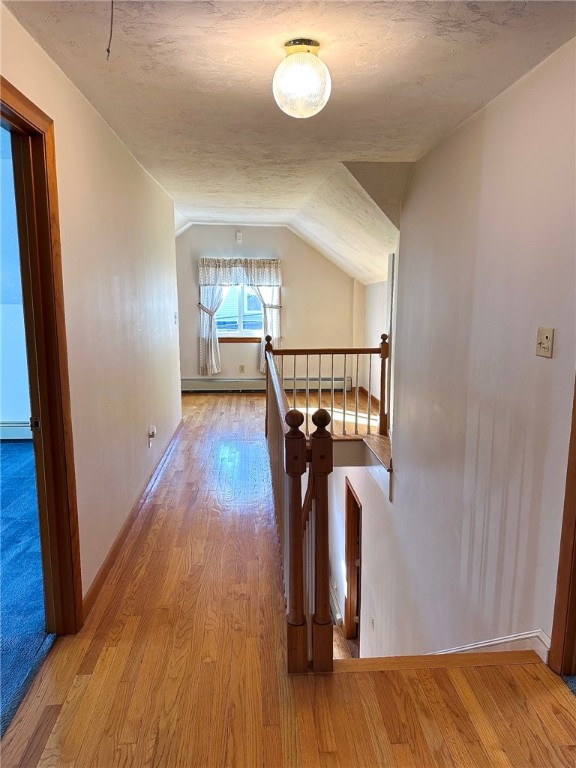 corridor with wood finished floors, baseboards, vaulted ceiling, an upstairs landing, and baseboard heating