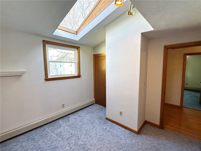 interior space with baseboard heating, vaulted ceiling with skylight, carpet flooring, and baseboards