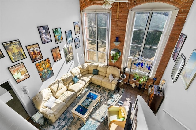 living area featuring wood finished floors, a healthy amount of sunlight, brick wall, and ceiling fan