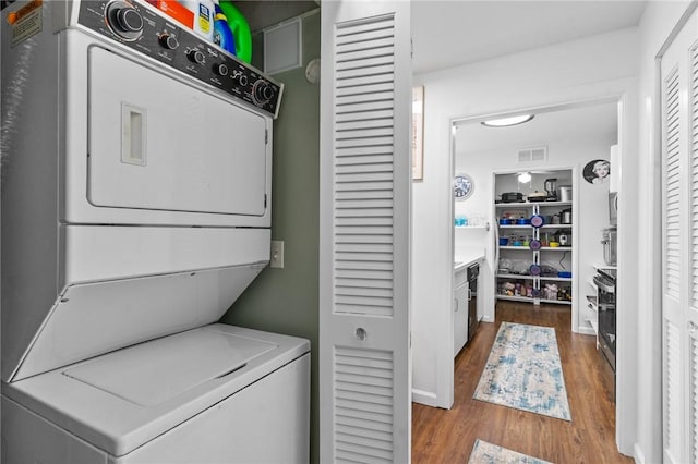 laundry area with stacked washer / dryer, laundry area, visible vents, and wood finished floors