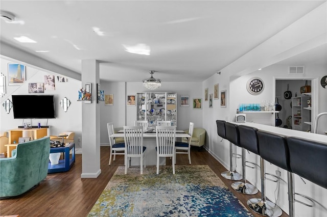 dining room featuring indoor wet bar, visible vents, baseboards, and wood finished floors