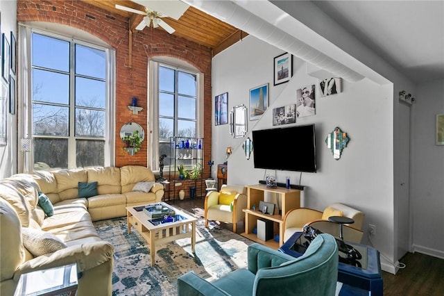 living area with wood finished floors, a towering ceiling, wooden ceiling, brick wall, and ceiling fan