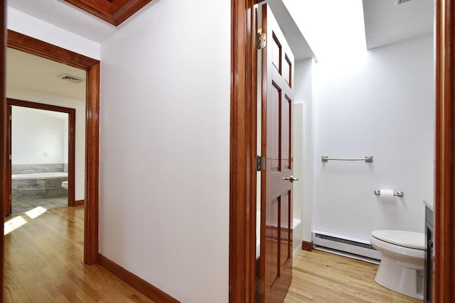 hall with a baseboard radiator, baseboards, visible vents, and light wood-style flooring