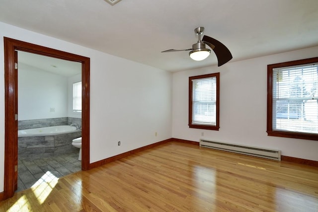 unfurnished room with plenty of natural light, baseboard heating, light wood-style flooring, and a ceiling fan