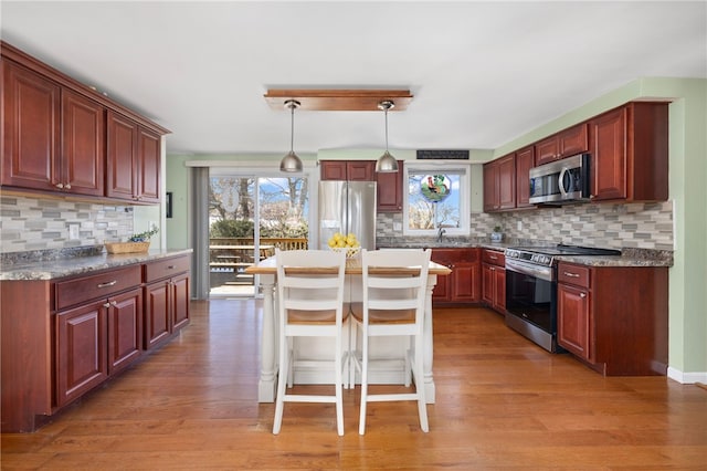 kitchen with light wood-type flooring, pendant lighting, a kitchen breakfast bar, tasteful backsplash, and appliances with stainless steel finishes