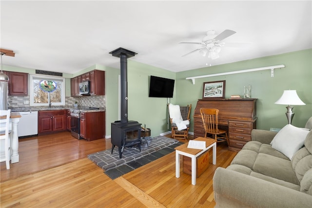 living room with a ceiling fan, light wood-style flooring, and a wood stove