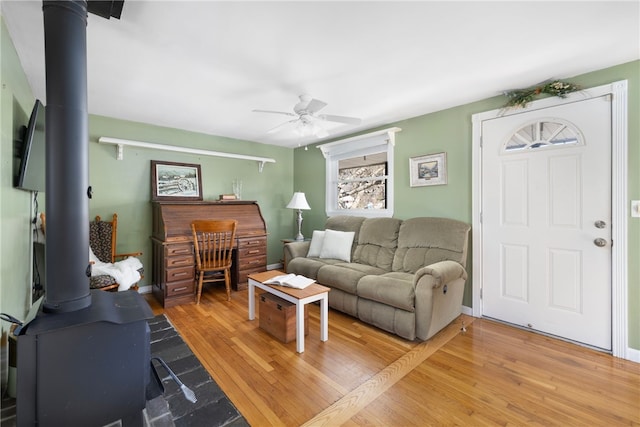 living area with ceiling fan, baseboards, a wood stove, and light wood-style floors