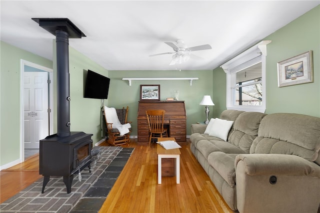 living room with baseboards, a ceiling fan, wood finished floors, and a wood stove