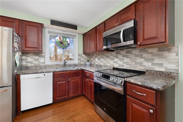 kitchen featuring light wood-style flooring, a sink, dark brown cabinets, appliances with stainless steel finishes, and backsplash