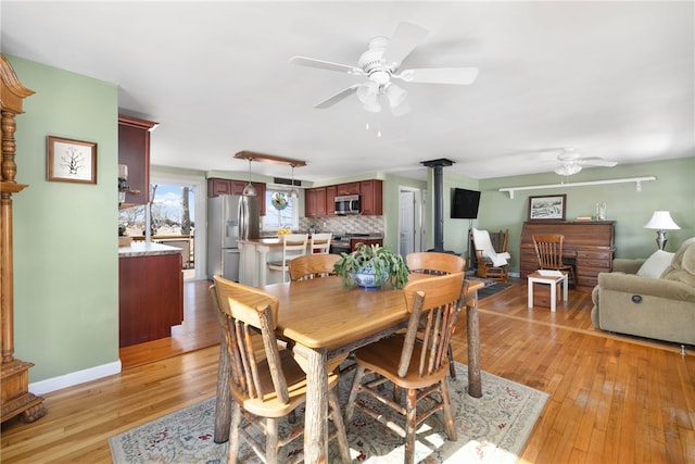 dining space with light wood finished floors, baseboards, a wood stove, and a ceiling fan