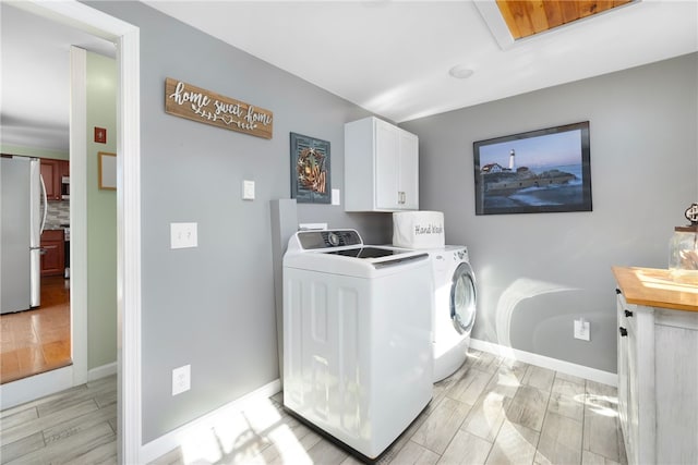 laundry room with wood finish floors, cabinet space, baseboards, and washing machine and clothes dryer