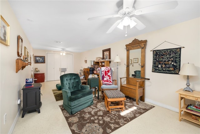 living room featuring baseboards, a ceiling fan, and a wood stove