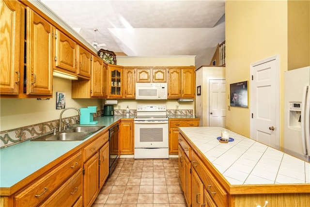 kitchen featuring tile counters, brown cabinetry, white appliances, a ceiling fan, and a sink