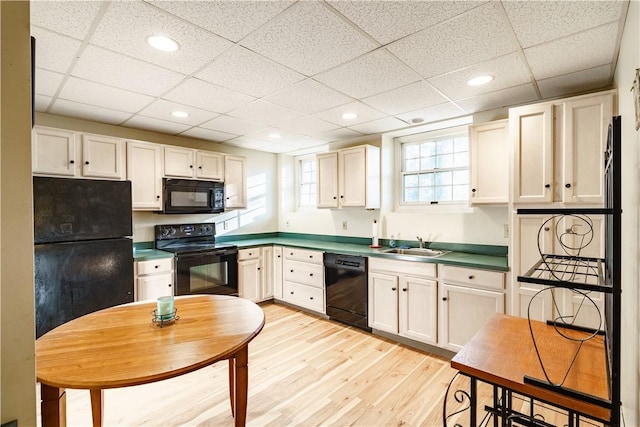 kitchen featuring a drop ceiling, recessed lighting, light wood-style flooring, black appliances, and a sink