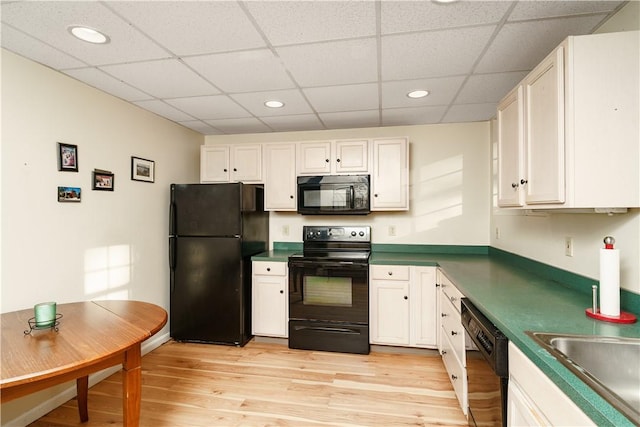 kitchen with light wood-type flooring, dark countertops, black appliances, and white cabinets