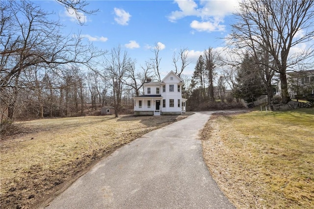 view of front of property featuring aphalt driveway, a porch, a chimney, and a front lawn