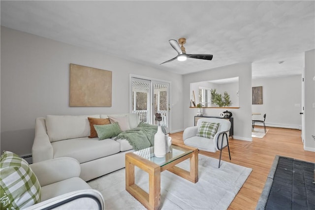 living room with ceiling fan, a baseboard heating unit, baseboards, and wood finished floors