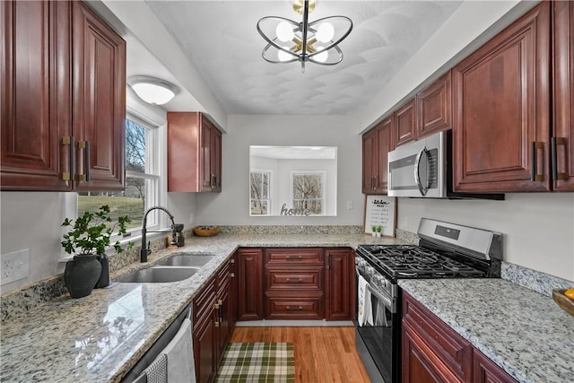 kitchen with a sink, light stone counters, light wood-style flooring, appliances with stainless steel finishes, and reddish brown cabinets