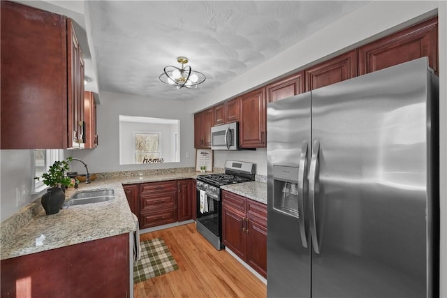 kitchen with a sink, light stone counters, light wood-style floors, stainless steel appliances, and reddish brown cabinets