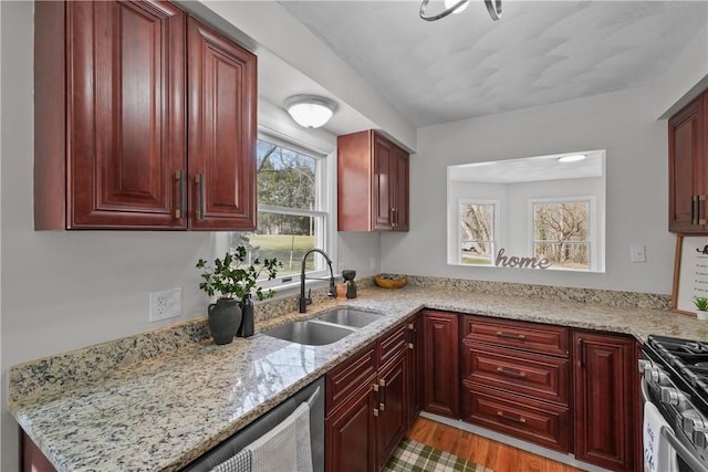 kitchen with light stone counters, light wood-style flooring, stainless steel appliances, a sink, and reddish brown cabinets