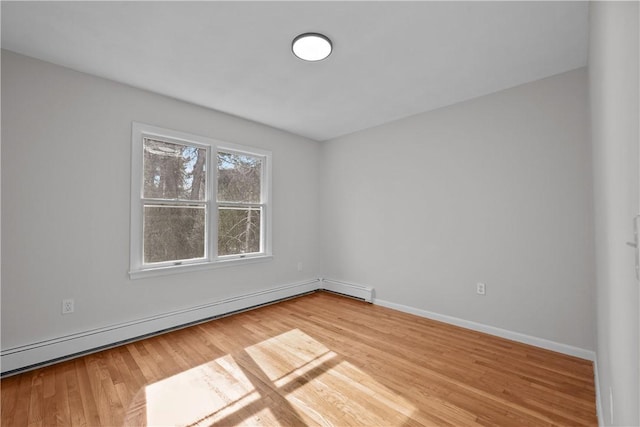 empty room featuring a baseboard heating unit, baseboards, and light wood-style flooring