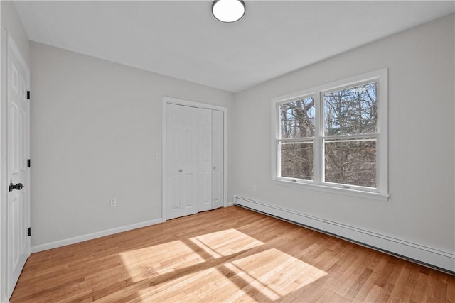 unfurnished bedroom featuring light wood-type flooring, a baseboard radiator, baseboards, and a closet