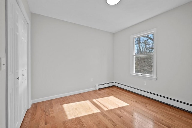 unfurnished bedroom featuring wood finished floors, a closet, baseboard heating, and baseboards