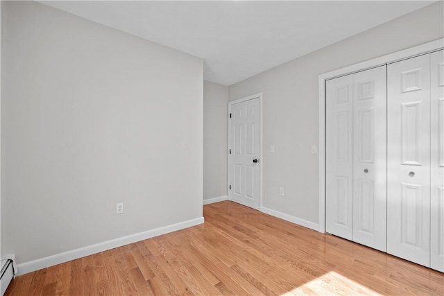 unfurnished bedroom with light wood finished floors, baseboard heating, a closet, and baseboards