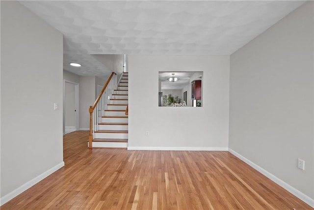 unfurnished living room featuring stairs, light wood-style flooring, and baseboards