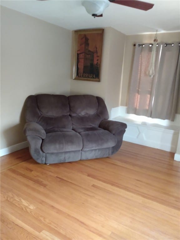 living area with baseboards, wood finished floors, and a ceiling fan