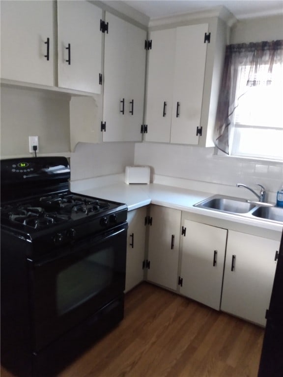 kitchen with black gas range oven, light countertops, wood finished floors, white cabinets, and a sink