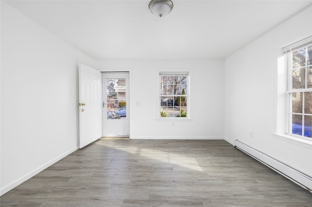 unfurnished room featuring a baseboard heating unit, baseboards, a healthy amount of sunlight, and wood finished floors