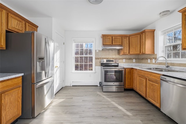 kitchen featuring tasteful backsplash, a baseboard heating unit, under cabinet range hood, stainless steel appliances, and a sink