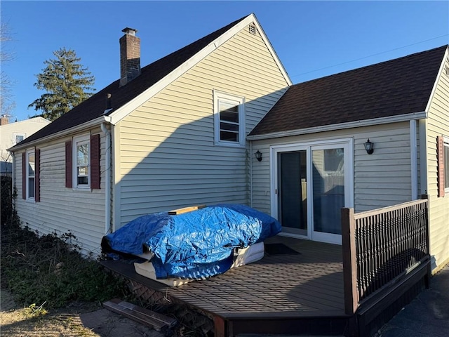 back of house featuring roof with shingles, a deck, and a chimney