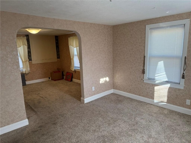 carpeted empty room featuring wallpapered walls, baseboards, and arched walkways