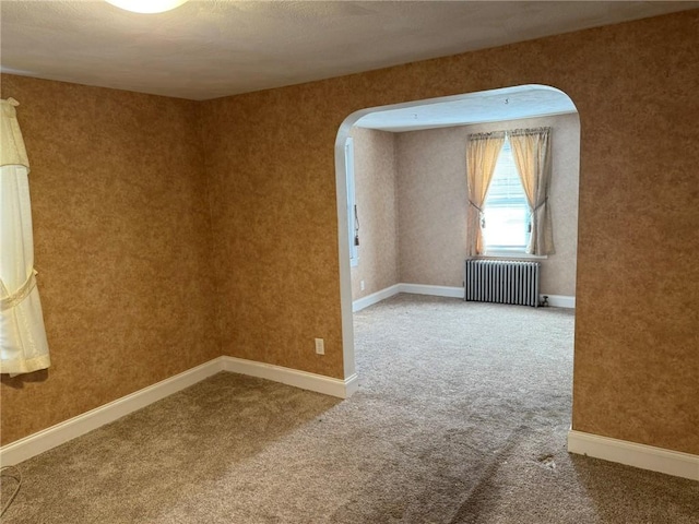 spare room with arched walkways, radiator, baseboards, and carpet